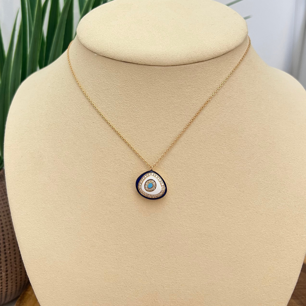 Necklace with a circular pendant on a beige bust against a white background with greenery.
